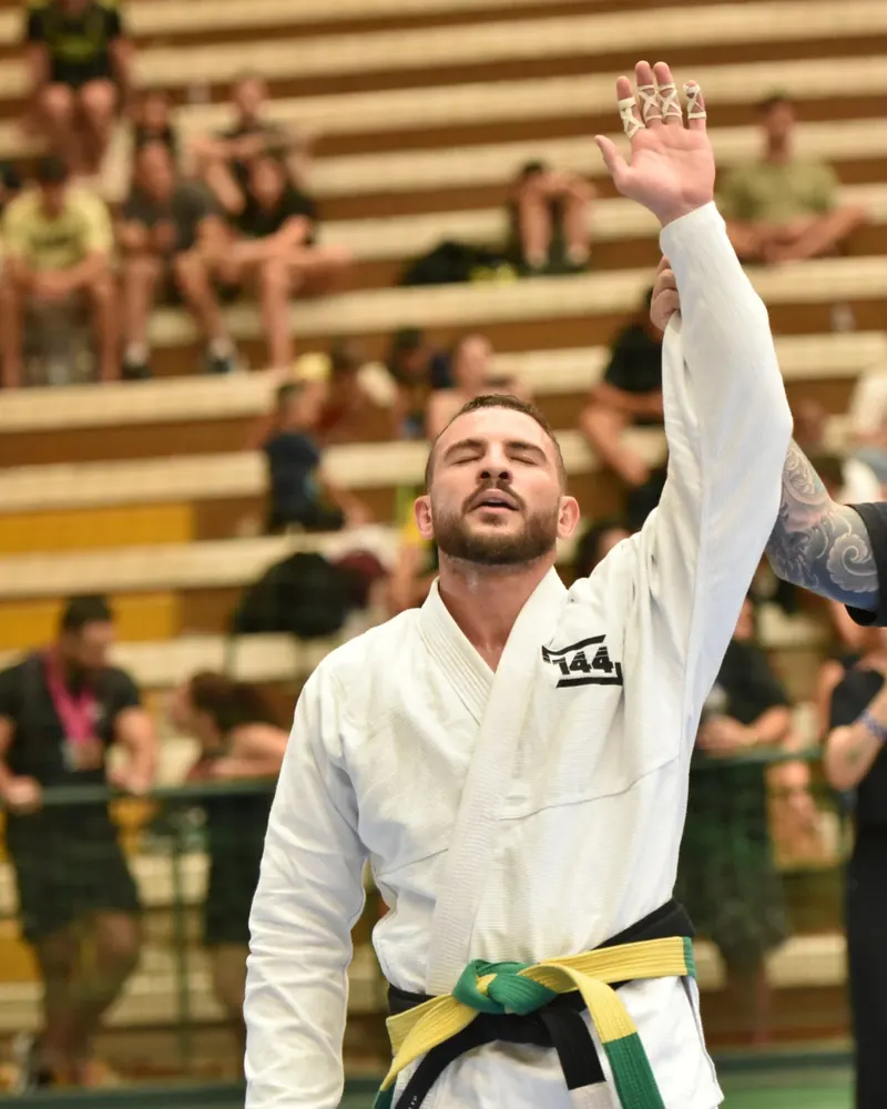 Gabriel Neves de kimono branco com o braço levantado após vencer uma luta